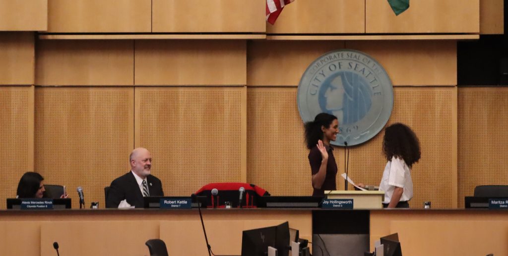 Foster is a black woman standing on the Council dais in front of the City of Seattle seal.