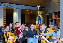 Urbanist Podcast: New Year, New Mayor, New Budget Wilson supporters hold yellow "This is your city" signs. She stands at the lectern and and a man adjust the mic to her height.