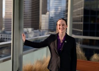 One Week In, Katie Wilson Charts the Path Ahead Wilson wears a black blazer and stands on the balcony outside her seventh floor office, with the downtown skyline in the background