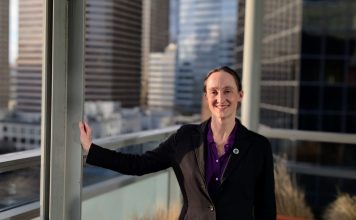 One Week In, Katie Wilson Charts the Path Ahead Wilson wears a black blazer and stands on the balcony outside her seventh floor office, with the downtown skyline in the background