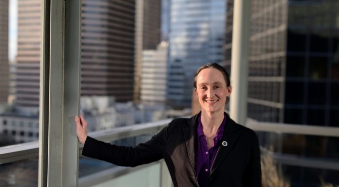 One Week In, Katie Wilson Charts the Path Ahead Wilson wears a black blazer and stands on the balcony outside her seventh floor office, with the downtown skyline in the background