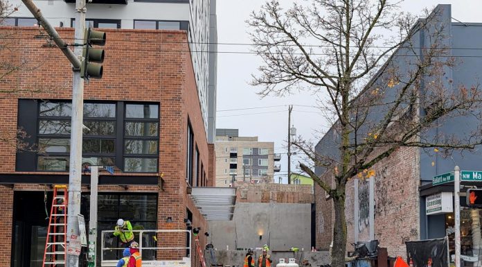 Wilson Promotes Sam Steele to Lead Seattle Permitting Department A half dozen hard-hatted construction workers work at a site between two midrise buildings on Ballard's Market Street.