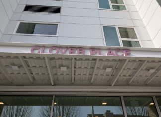 Supportive Housing Building Opens Near Seattle’s Woodland Park The metal awning includes the building name in red letters. The building has a white facade.