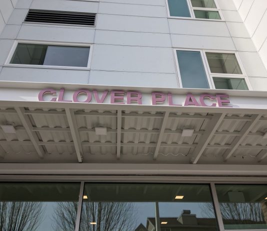 Supportive Housing Building Opens Near Seattle’s Woodland Park The metal awning includes the building name in red letters. The building has a white facade.