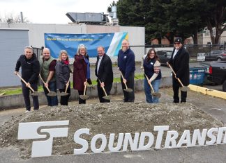 Sound Transit Breaks Ground on Stride S3 Bothell-to-Shoreline Bus Line Eight Sound Transit leaders lift a shovelful of ceremonial dirt next to an agency logo and poster board