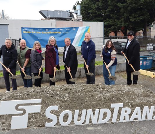 Sound Transit Breaks Ground on Stride S3 Bothell-to-Shoreline Bus Line Eight Sound Transit leaders lift a shovelful of ceremonial dirt next to an agency logo and poster board