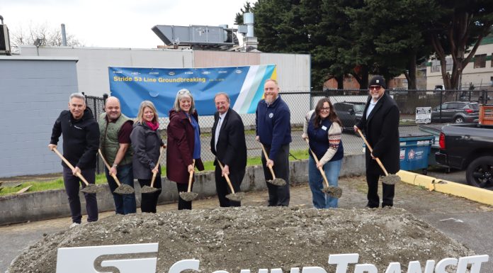 Sound Transit Breaks Ground on Stride S3 Bothell-to-Shoreline Bus Line Eight Sound Transit leaders lift a shovelful of ceremonial dirt next to an agency logo and poster board