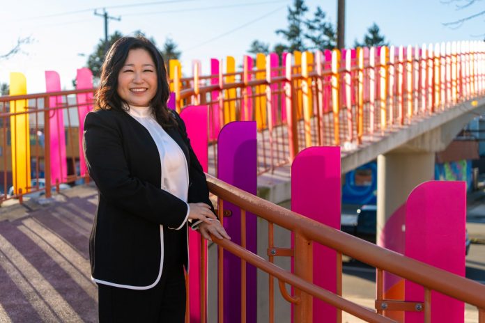 Kang stands by a colorful pedestrian bridge over Aurora Avenue.