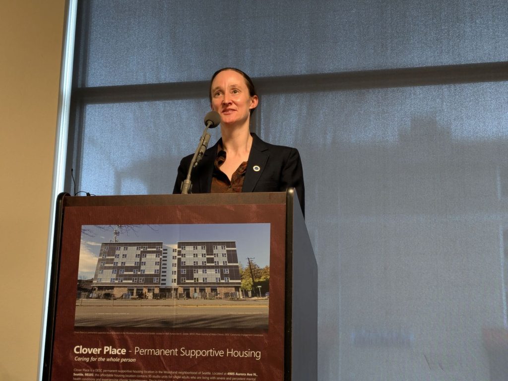 Wilson stands at a big lectern displaying a picture of the building's exterior.