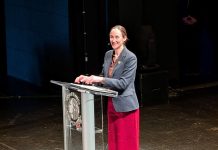 Wilson Sketches Affordability Agenda in State of City Speech Wilson smiles and stands at a lectern with the City seal. She wears a red skirt and gray blazer.