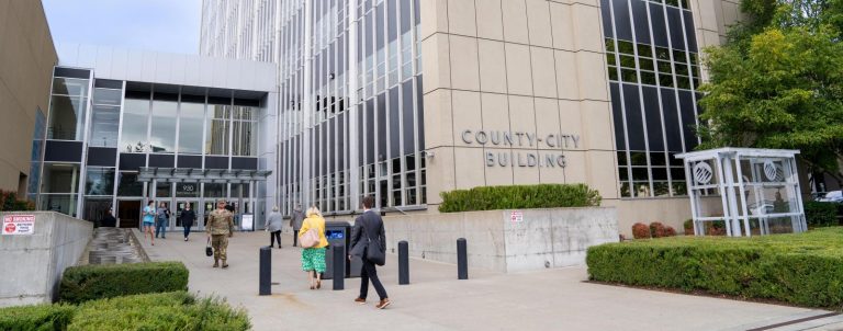 A stream of people in formal clothes walk into a modern concrete and plate class courthouse building