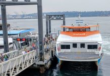 Mosquito Fleet Act Runs Into Choppy Seas in the State Senate Passengers load onto a orange and white Kitsap fast ferry boat with Elliott Bay in the background.