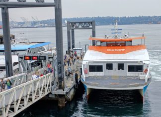 Mosquito Fleet Act Runs Into Choppy Seas in the State Senate Passengers load onto a orange and white Kitsap fast ferry boat with Elliott Bay in the background.