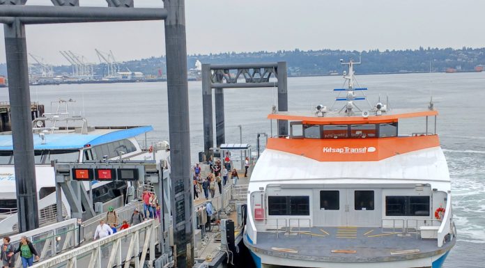 Mosquito Fleet Act Runs Into Choppy Seas in the State Senate Passengers load onto a orange and white Kitsap fast ferry boat with Elliott Bay in the background.