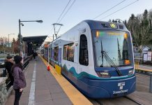 Op-Ed: Finding Smart Solutions to Sound Transit Budget Woes Riders wait as a train pulls into Columbia Station Station, which in the median of a four-lane road.