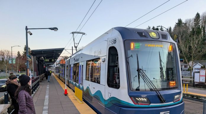 Op-Ed: Finding Smart Solutions to Sound Transit Budget Woes Riders wait as a train pulls into Columbia Station Station, which in the median of a four-lane road.